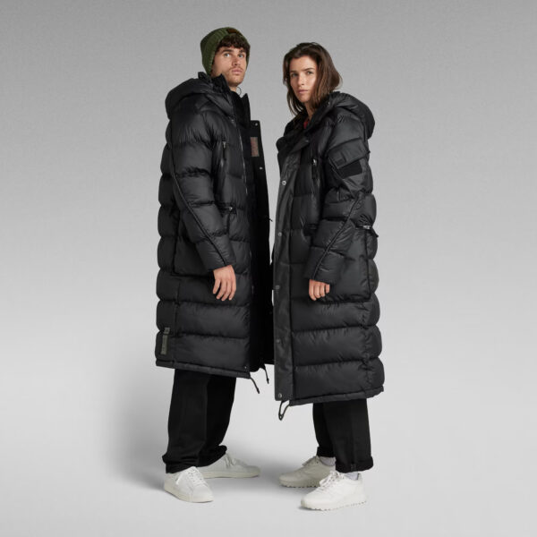 VESTE UNISEX EXTRA LONG PUFFER Cette doudoune ultra longue est dotée d’une grande capuche avec un col montant et une visière allongée. Des poches zippées sont positionnées à la poitrine et à la taille. Sur l’une des manches, une poche à rabat dotée d’un support pour écusson sur le haut a été créée